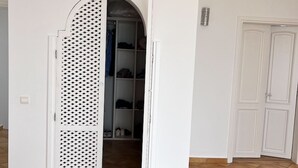 Huone, jossa on laattalattia, valkoinen ovi ja hyllyillä varustettu vaatekaappi.