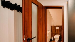 Une porte en bois donne sur une salle de bain équipée de toilettes, d’une serviette et d’un rouleau de papier toilette.
