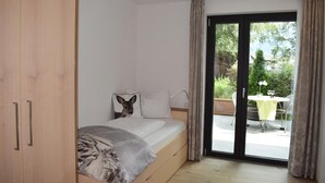 Un dormitorio con cama, armario y puerta corrediza de vidrio que da a un área exterior con mesa y sillas.