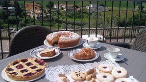 Et bord med et udvalg af kager og en tærte, placeret på en balkon med udsigt over et smukt landskab.