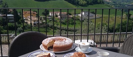 A table with a variety of pastries and a pie, set on a balcony overlooking a scenic landscape.