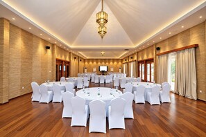Un salón de conferencias con mesas redondas, sillas blancas y una pantalla grande al frente.