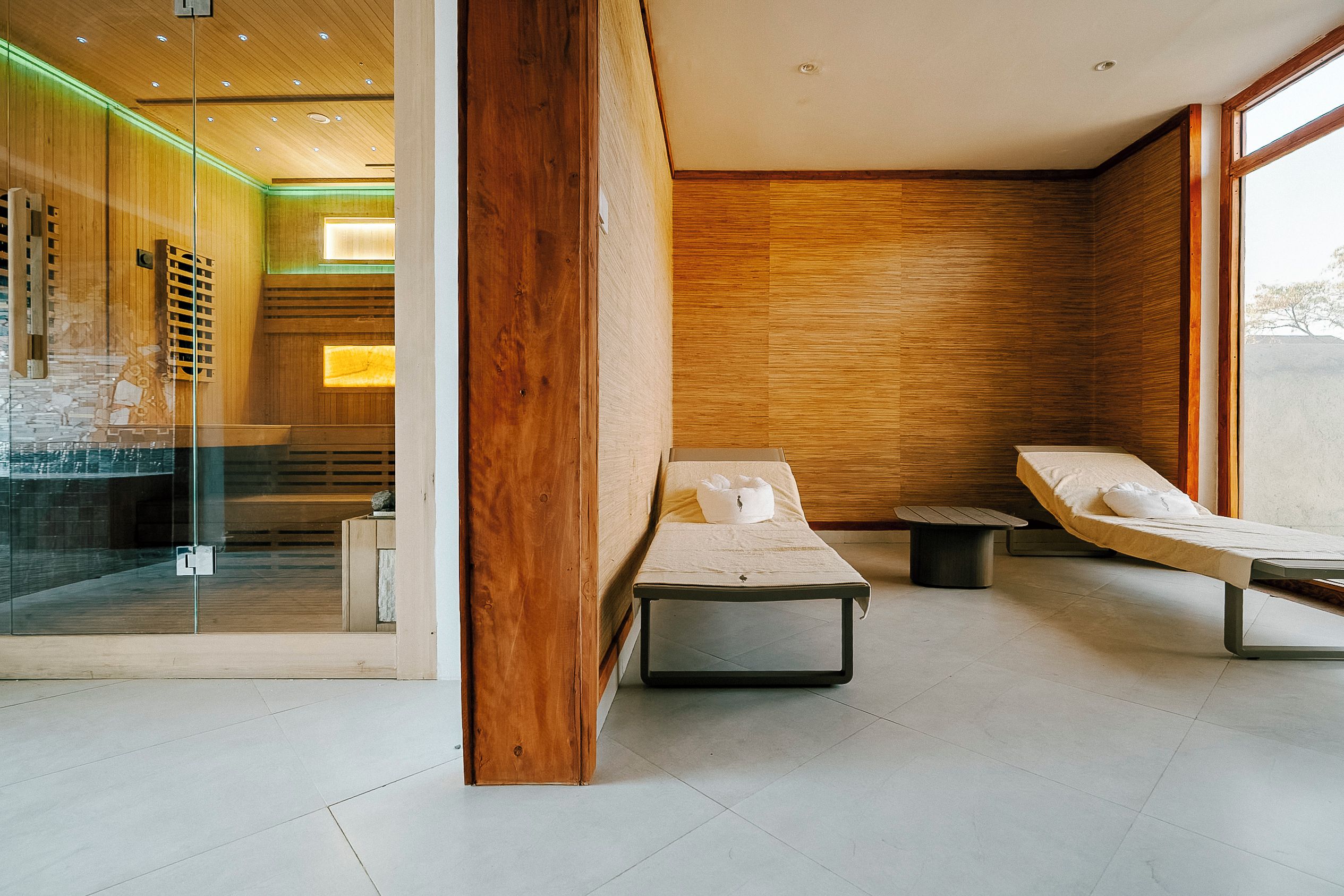 Un moderno cuarto de spa con dos camillas, una mesita y una pared de vidrio.