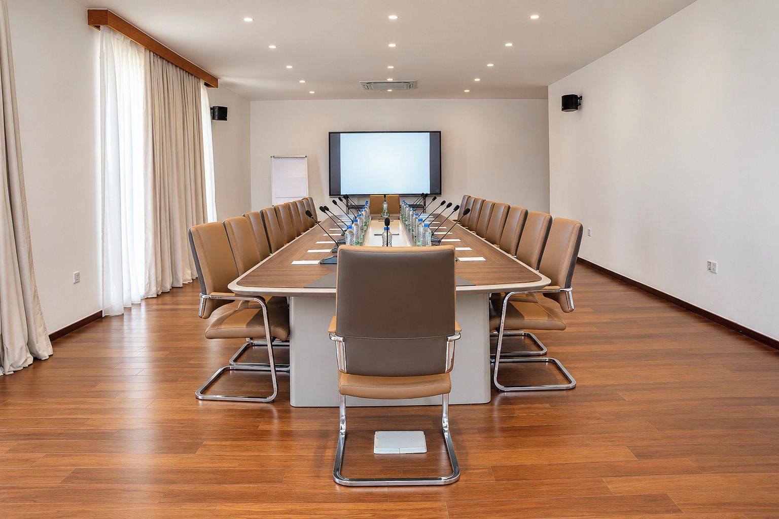 Uma sala de conferência com uma mesa comprida, cadeiras, tela de projetor e quadro branco.