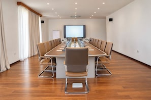 A conference room with a long table, chairs, a projector screen, and a whiteboard.