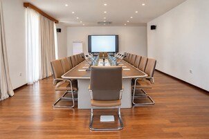 Un salón de conferencias con una larga mesa, sillas, una pantalla de proyector y una pizarra.
