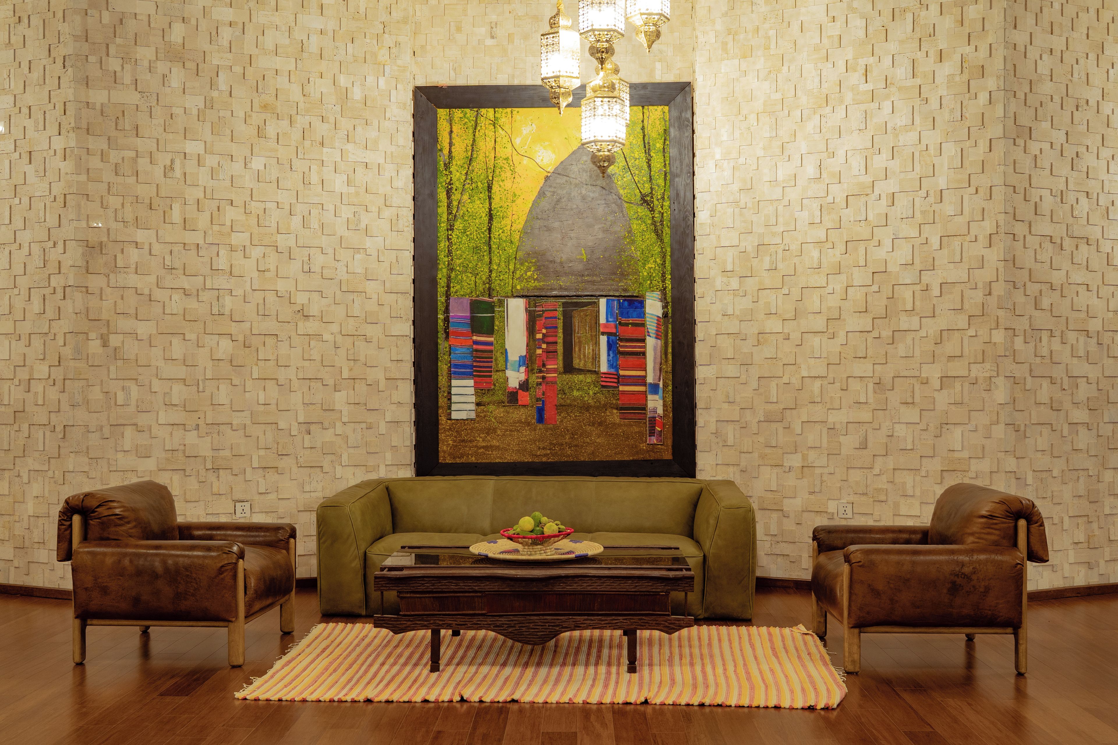 Una habitación con pared estampada, un sofá verde, dos sillones de cuero, una mesa de centro de madera y una obra de arte enmarcada.