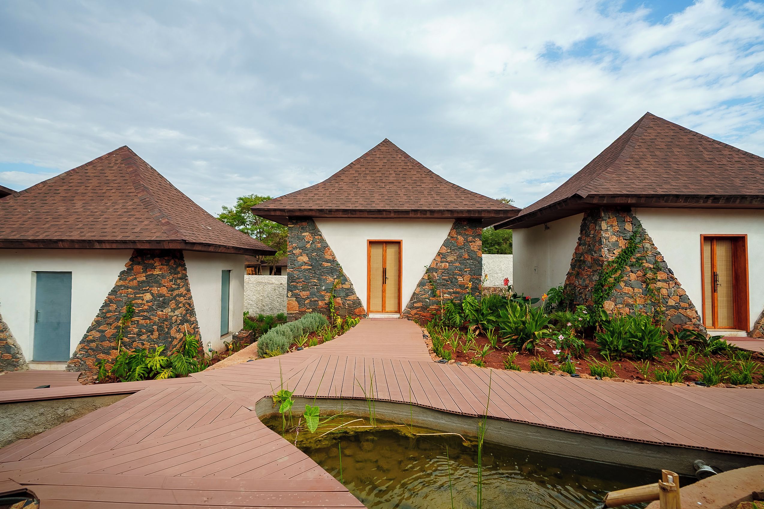 A row of three bungalow-style buildings with pitched roofs, a central pathway, and a small water feature.