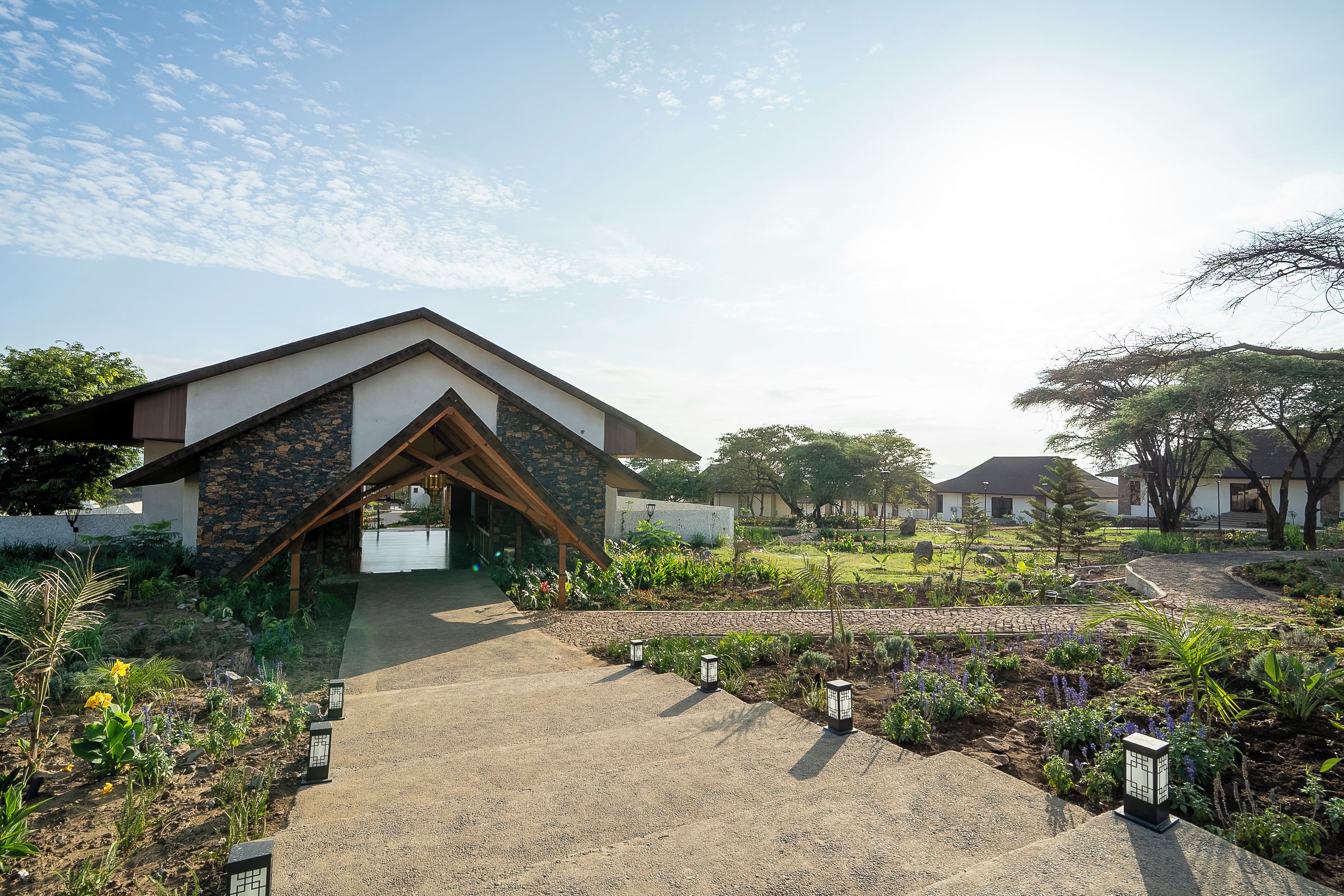 A modern building with a sloped roof and a stone facade, surrounded by a landscaped garden with pathways and outdoor lighting.