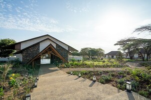 Um edifício moderno com telhado inclinado e fachada de pedra, rodeado por um jardim ajardinado com caminhos e iluminação externa.