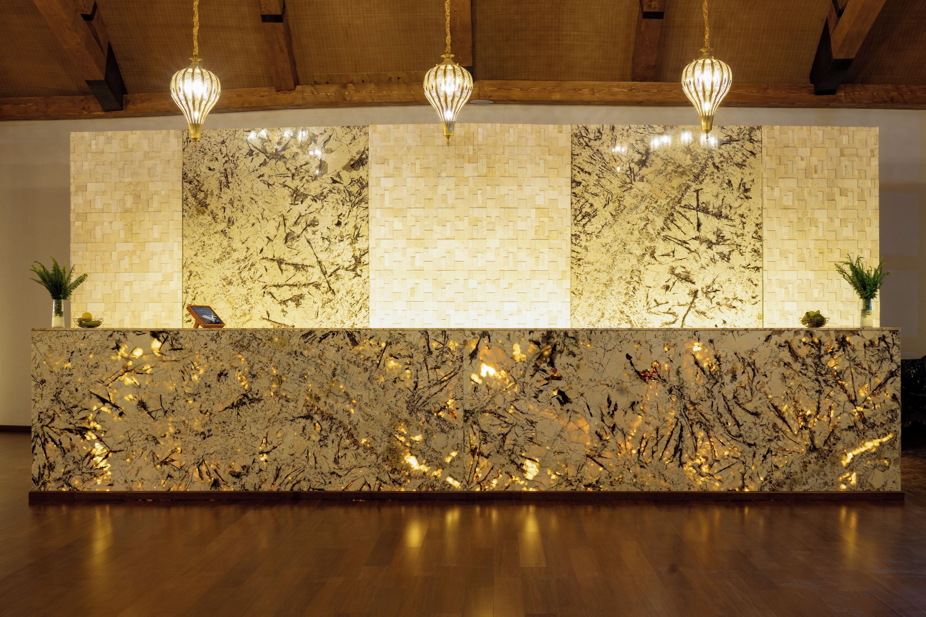 A reception desk with a marble top, wooden paneling on the wall, and hanging pendant lights.