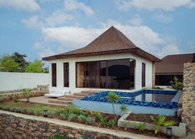 Una casa moderna con piscina, un patio con asientos y un muro de piedra.
