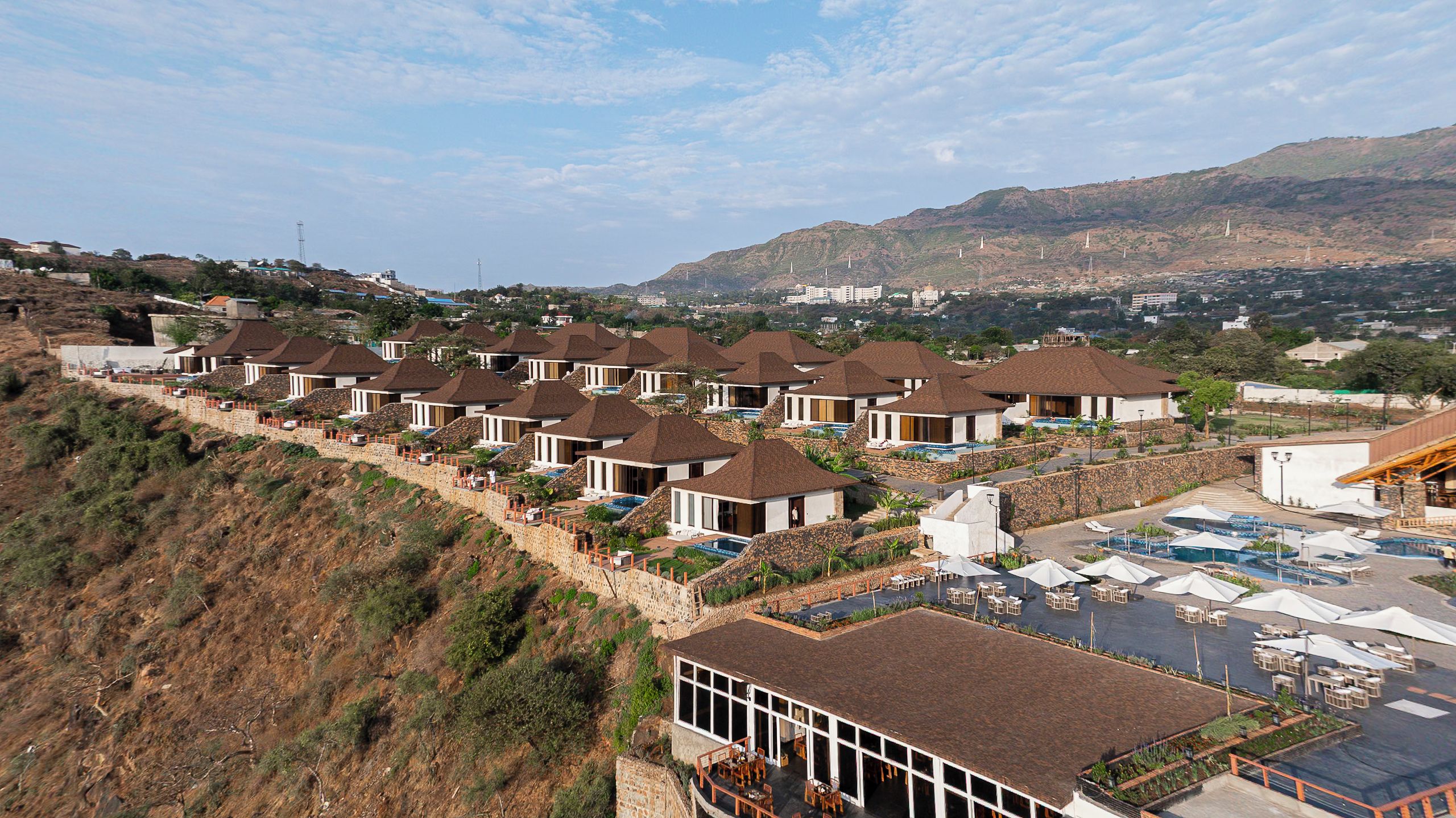 Un complejo turístico con varias edificaciones tipo bungaló, una zona de piscina y vistas del paisaje circundante.