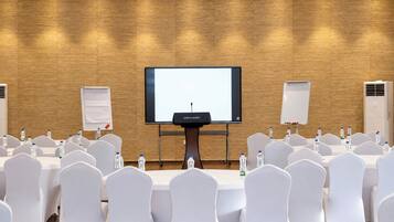 A conference room with a large screen, white chairs, tables, and water bottles.