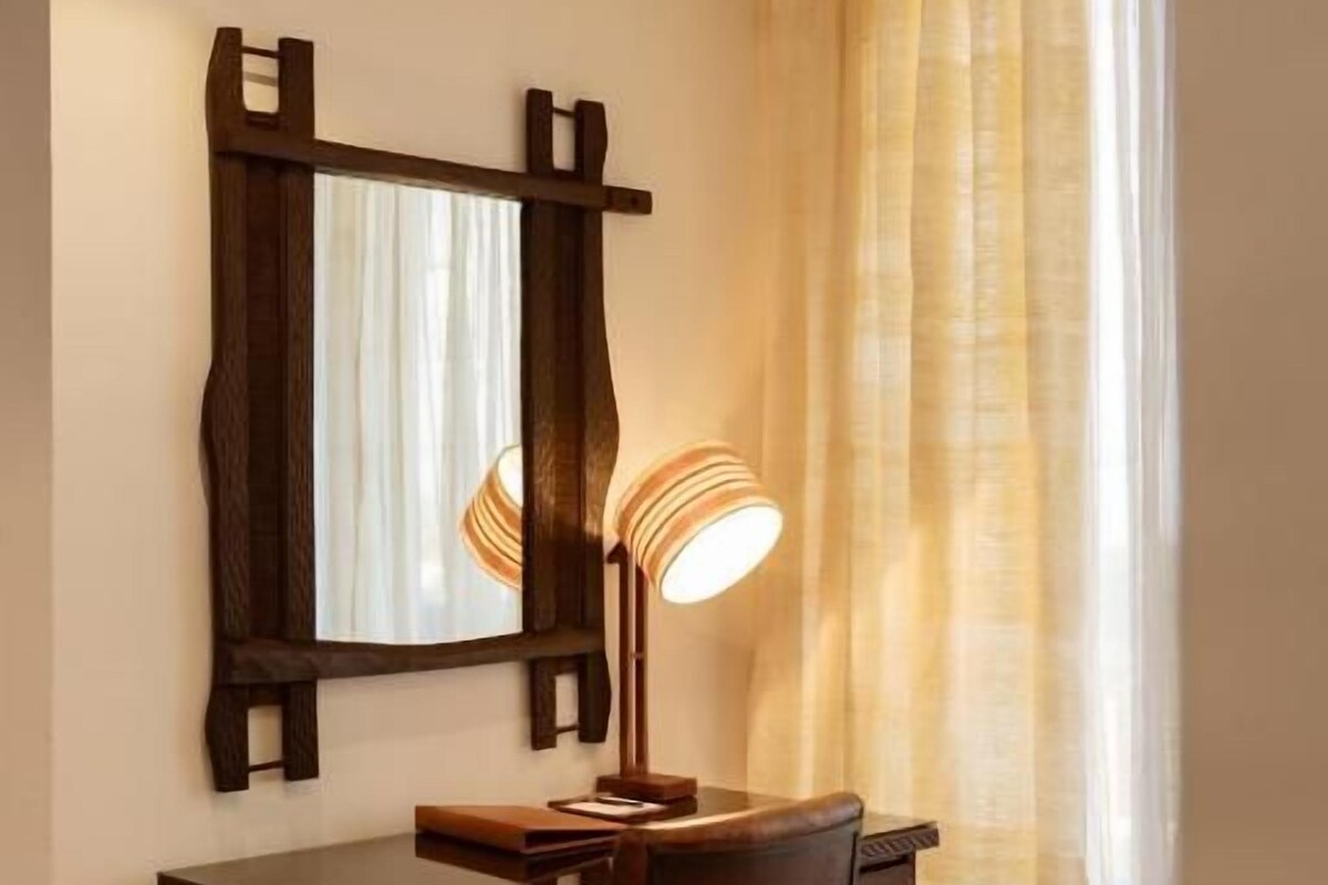 A room with a wooden desk, a chair, a mirror, and a lamp.