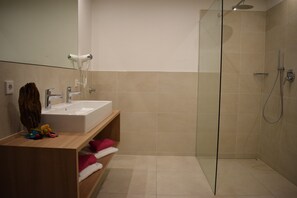 Een moderne badkamer met een douchecabine van glas, een wastafel en een aan de muur bevestigde haardroger.