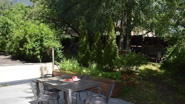 An outdoor dining area with a table and chairs, surrounded by greenery and a view of a building in the background. - Apartment 'Residence Ladurn Herz' with Mountain View, Balcony and Wi-Fi (Tirol)