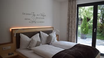 Un dormitorio con cama, almohadas, una mesita de noche, una pared con una cita inspiradora y vistas a la vegetación a través de una ventana.