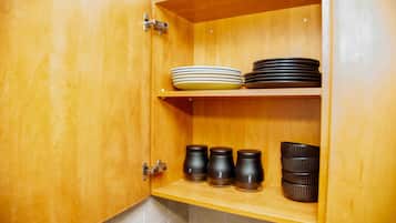 A wooden kitchen cabinet with two shelves; the top shelf holds stacked plates, and the bottom shelf contains black mugs.
