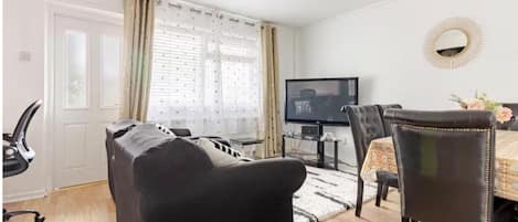 A living room with a sofa, a television, and a dining area with chairs and a table.