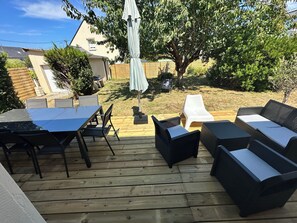 Eine Terrasse mit Tisch und Stühlen, ein weißes Liegestuhl und Korbmöbel.