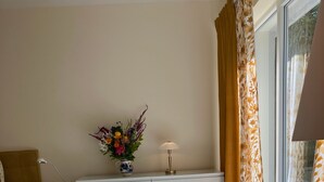 A room with a sofa, a small round table, a lamp, and a vase with flowers on a white console table.
