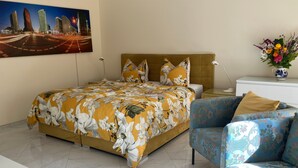A hotel room with a bed, a chair, a nightstand, a lamp, and a painting of city buildings.