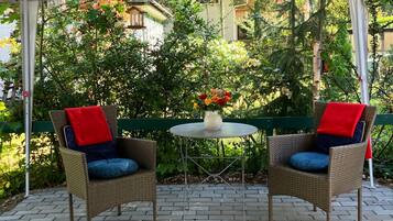 Ein überdachter Patio-Bereich mit zwei Korbstühlen, einem kleinen runden Tisch und einem Blumenstrauß.