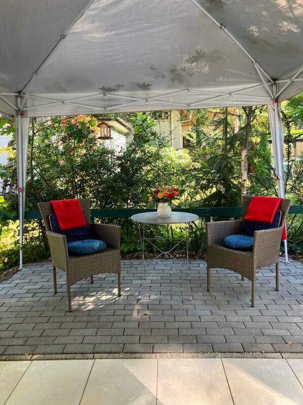A covered patio area with two wicker chairs, a small round table, and a vase of flowers.