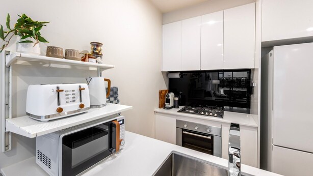 Una cucina moderna con mobili bianchi, forno integrato, microonde, macchina del caffè e tostapane.