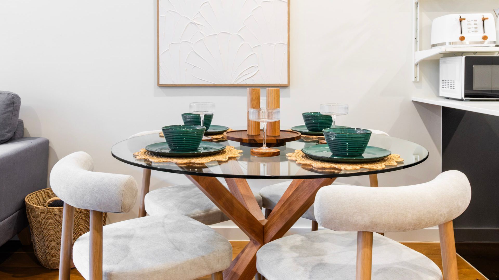 A round glass table with a wooden base, surrounded by four white cushioned chairs.