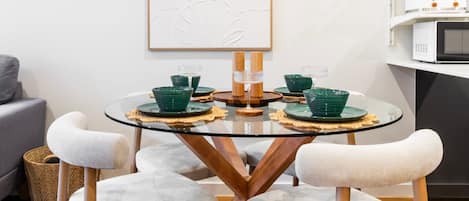 A round glass table with a wooden base, surrounded by four white cushioned chairs.