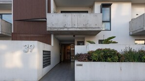 Un edificio moderno con facciata in cemento, un ingresso ben visibile e una piccola area giardino con piante.
