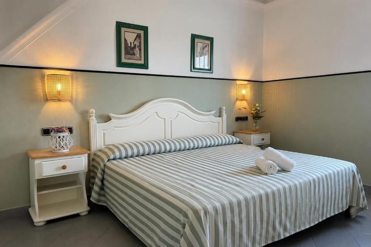 A neatly made bed with striped bedding, two bedside tables with lamps, and framed pictures on the wall.