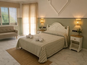 A bedroom with a bed, bedside tables, a nightstand, a sofa, and a window with blinds.