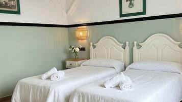 Habitación de hotel con dos camas, una mesita de noche con lámpara e impresión botánica enmarcada en la pared.