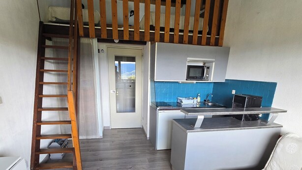 Um espaço compacto com cozinha compacta, um sofá, uma mesa de centro e uma escada de madeira.