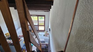 Quarto com estrutura de teto em madeira, parede branca e vista para uma varanda com grade de madeira.