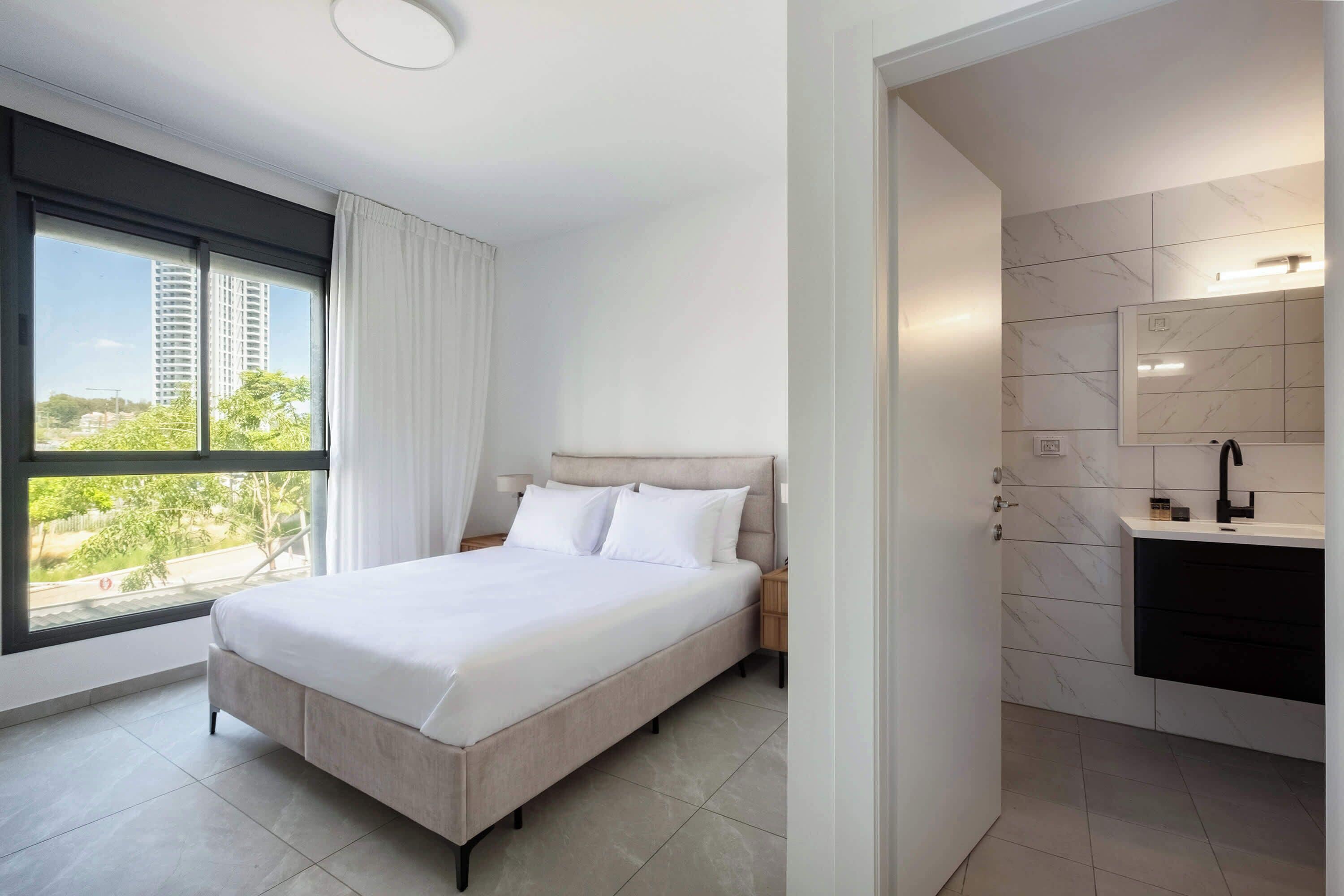 Restful bedroom featuring a split Jewish bed, crisp white linens, modern ensuite access, and soft filtered daylight.