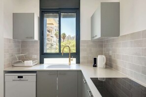 Una cocina moderna con lavavajillas integrado, una ventana con vistas a edificios y una cafetera sobre la encimera.