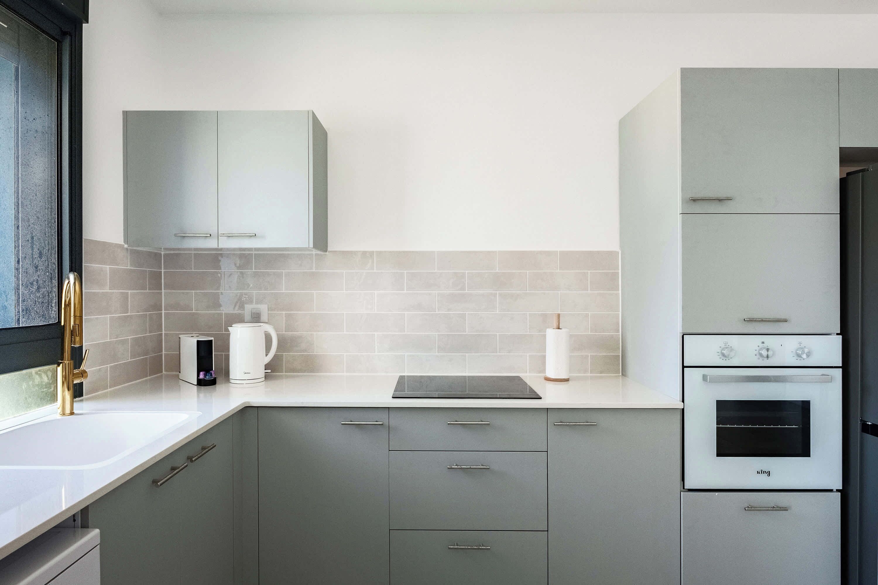 Una cocina moderna con gabinetes grises, un horno empotrado y una cafetera sobre la encimera.