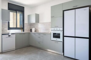 A modern kitchen with grey cabinets, a dishwasher, an oven, and a double-door refrigerator. - Elegant 4BR Stay l Balcony & Mamad (Bat Yam)