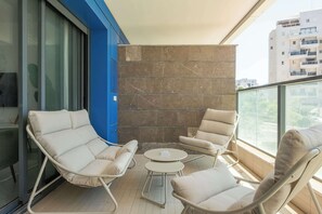 A balcony with two lounge chairs, a small round table, and a stone wall. - Elegant 4BR Stay l Balcony & Mamad (Bat Yam)