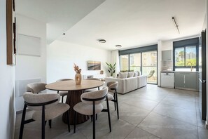 A modern living space with a dining area, a sofa set, and a kitchen. - Elegant 4BR Stay l Balcony & Mamad (Bat Yam)