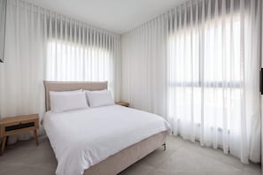 Une chambre à coucher avec un lit, des tables de chevet et des rideaux légers.