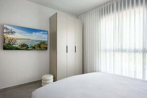 Un dormitorio con cama, armario, taburete pequeño y un cuadro de un paisaje costero.