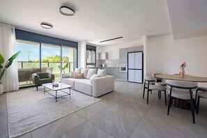 A modern living room with a sofa, coffee table, and a dining area with chairs and a table. - Elegant 4BR Stay l Balcony & Mamad (Bat Yam)