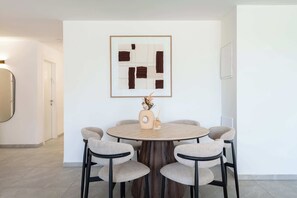A round dining table with six chairs, a vase with dried flowers, and a framed abstract painting on the wall. - Elegant 4BR Stay l Balcony & Mamad (Bat Yam)