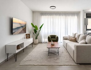 Un saló modern amb un sofà, una taula de centre, una televisió, una planta i una finestra amb cortines.