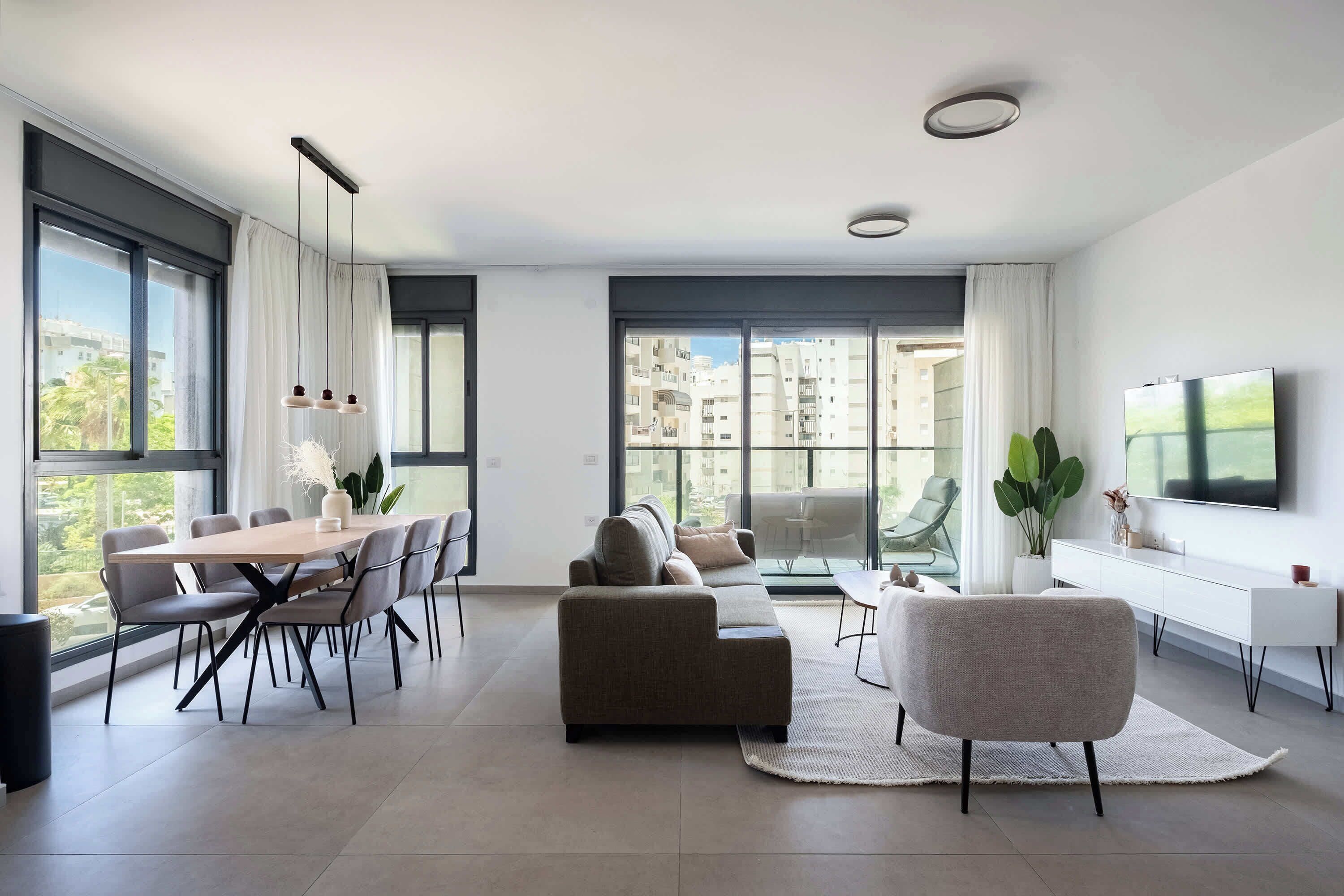 Expansive living area with multiple windows, integrated dining space, comfortable seating, and light wood flooring.
